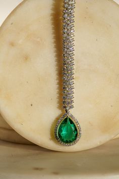 Enhance your elegance with the Safi Diamanté Accent Maang Tikka, a radiant piece crafted in a rhodium-plated silver finish. Available in stunning emerald green or sapphire blue, this exquisite maang tikka features a paved setting with glistening white diamante AD stones complemented by teardrop-shaped stones in your chosen hue. Its smaller size ensures a flattering fit for all face sizes, designed perfectly to complement our Sharmine necklace set. Key Features: Elegant Design: Paved setting with Emerald Maang Tikka, Emerald Drop Jewelry With 17 Jewels, Green Cubic Zirconia Jewelry For Evening, Evening Green Cubic Zirconia Jewelry, Glamorous Green Teardrop Jewelry, May Birthstone Party Jewelry, Fine Jewelry For Party With Emerald, Fine Jewelry For Parties With Emerald Accents, White Gold Teardrop Jewelry For Party