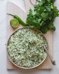 a wooden cutting board topped with a bowl filled with rice and cilantro leaves