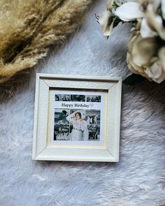 a happy birthday photo frame sitting on top of a fur covered floor next to flowers