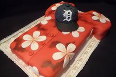 a baseball cap on top of a red and white cake with flowers in the middle