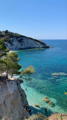 people are swimming in clear blue water near the cliffs and trees on top of them