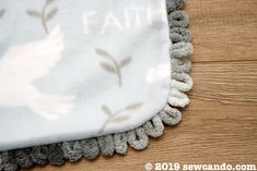 a close up of a white and gray blanket on a wooden floor with the word faith printed on it