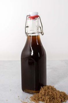 a bottle filled with brown stuff sitting on top of a white counter next to a pile of dirt