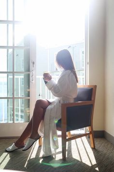 a woman sitting in a chair with her legs crossed looking out the window while holding a cell phone