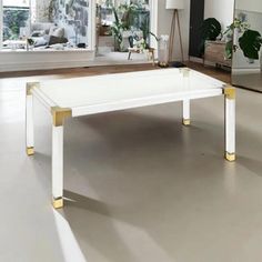 a white coffee table with gold legs in front of two large windows and mirrors on the wall