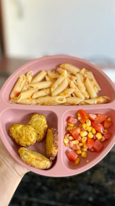 a person holding a pink plate with different foods in it, including pasta and veggies