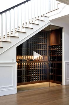 an open wine cellar under the stairs in a room with wooden floors and white railings