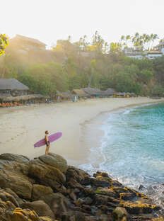 a man holding a surfboard on top of a sandy beach next to the ocean