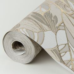 a white and gold wallpaper with floral design on the bottom half of it, next to a roll of tape