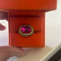 a person holding an orange ring with a pink stone in it's center on top of a red box