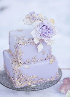 a three tiered cake with purple flowers on the top and gold trimmings