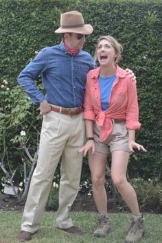 a man and woman standing next to each other in front of a hedge with their arms around each other