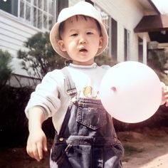 a young boy wearing overalls and a hat holding a white frisbee in front of a house