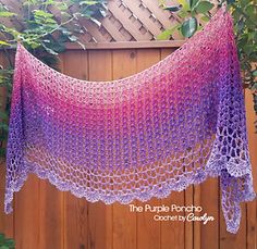 a purple and pink crocheted shawl hanging from a tree in front of a wooden fence