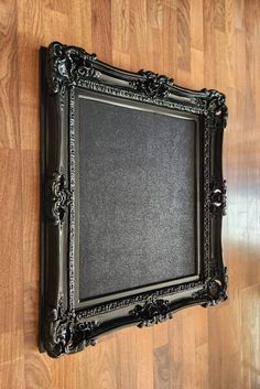 an old black frame on the floor with wood floors in the background and a wooden wall behind it