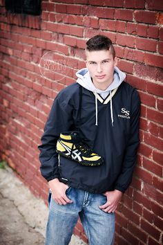 a young man leaning against a brick wall with his hands in his pockets and wearing a pair of sneakers