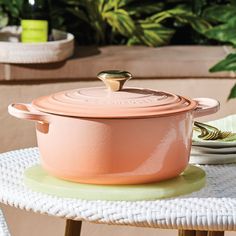 a pink pot sitting on top of a white table next to plates and plants in the background