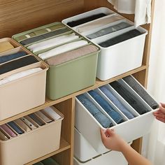 a person is reaching for some folded clothes in a storage unit with drawers and bins