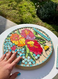 a hand is touching the top of a colorful flower mosaic on a white table outside