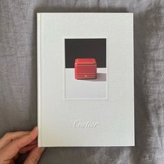 a hand holding an open book with a red object in the middle on a bed