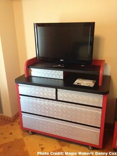 a flat screen tv sitting on top of a red and black dresser next to a wall