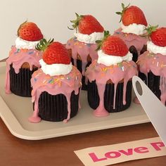 cupcakes decorated with strawberries and whipped cream on a plate next to a knife