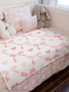 there is a bed with pink hearts on it and two stuffed animals in the corner