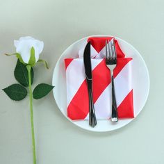 a white plate topped with a fork and knife next to a rose