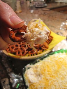 a person is holding up a hot dog in front of a bowl of cheese and pretzels