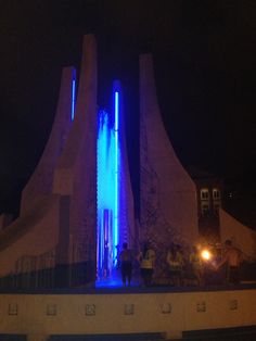 some people are standing in front of a building with blue lights on it at night