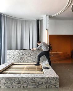 a man standing on top of a bed frame in a living room next to a window