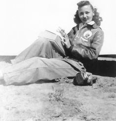 a woman sitting on the ground with her book in her hand and looking at the camera