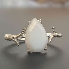 "For fans of minimalist nature-inspired jewelry, we created our stand-out Mother Nature Silver breastmilk ring. It pairs together a branch-like sterling silver ring band with an exquisite yet small pear-shaped faceted breastmilk stone. Go with your natural breast milk or combine your breast milk with opal effect flakes or pearl powder. Opalizing your breast milk adds a pale, milky opal appearance to your breastmilk stone that catches the light and reflects pastel rainbow hues, while adding pearl Minimalist White Moonstone Ring In Sterling Silver, Delicate White Moonstone Ring In Sterling Silver, White Hypoallergenic Moonstone Jewelry, Hypoallergenic White Moonstone Jewelry, Delicate White Moonstone Gemstone Ring, Delicate White Moonstone Ring, Minimalist White Moonstone Jewelry, Delicate White Moonstone Ring For Anniversary, Delicate White Hypoallergenic Ring