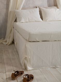 a pair of sandals sitting on the floor next to a bed with white sheets and drapes