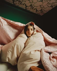 a woman wrapped in a blanket on top of a bed with pink sheets and pillows