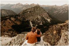 two people sitting on top of a mountain looking at the mountains