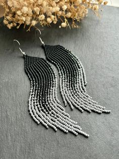 the black and white beaded fringe earrings are hanging from silver hooks on a gray surface