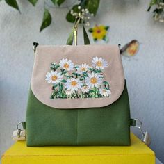 a green purse with white daisies on it sitting on top of a yellow box