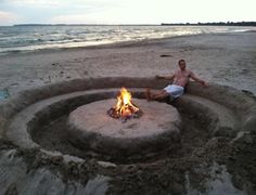 a man sitting in front of a fire pit on the beach