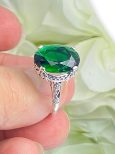 6ct. Simulated Emerald 925 Sterling Silver RingEdward Design#D70 This filigree ring is a reproduction of a sterling silver Edwardian antique with a simulated green emerald gemstone solitaire. This full cut oval gem is 14mm x 10mm. This ring sits 7mm off the finger. The inside of the band is marked 925 for sterling silver. Notice the beautiful leaf and floral design of the silver filigree setting and etched band. This ring is part of our Edward series, which includes bracelets, earring, and pendant necklaces. This is the original Edward design, with a generously cut gemstone that is accented above the filigree. This is a lovely rendition of an antique filigree ring. This amazing design is pure style and grace. You can dress it up or down, it's the perfect statement. Your every movement will Classic Green Jewelry With Vs Clarity, Green Sterling Silver Filigree Ring For Anniversary, Classic Green Filigree Ring With Gemstone, Green Oval Filigree Ring In Sterling Silver, Victorian Green Ring As A Gift, Classic Green Sterling Silver Filigree Ring, Green Sterling Silver Classic Filigree Ring, Elegant Stamped 925 Emerald Ring, Green Sterling Silver Filigree Ring