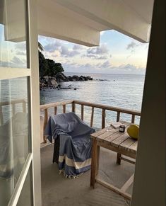 an open door leading to a balcony with a table and chairs on it, overlooking the ocean