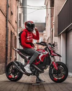 a man sitting on top of a red and black motorbike in an alley way