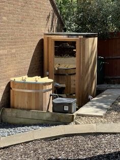 a wooden sauna outside in front of a brick building with gravel around it and a trash can next to it