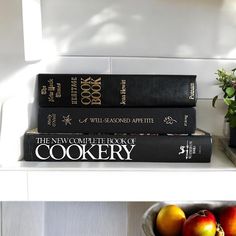 three books are stacked on top of each other in front of a bowl of fruit