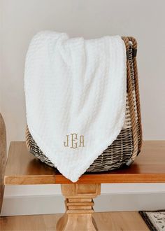 a white blanket sitting on top of a wooden table next to a basket with a monogrammed towel