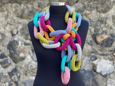 a multicolored knitted scarf on a mannequin headdress stands in front of a stone wall