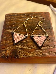 two triangle shaped beaded earrings sitting on top of a piece of wood