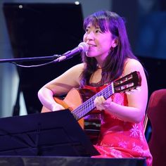 a woman sitting in front of a microphone while holding a guitar and singing into a microphone