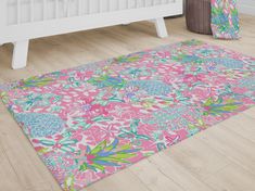 a pink and green floral rug on the floor next to a white crib bed