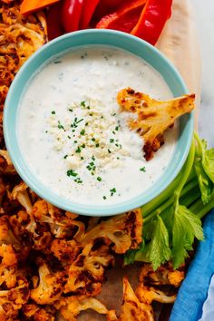 a blue bowl filled with white sauce next to some red peppers and other food items